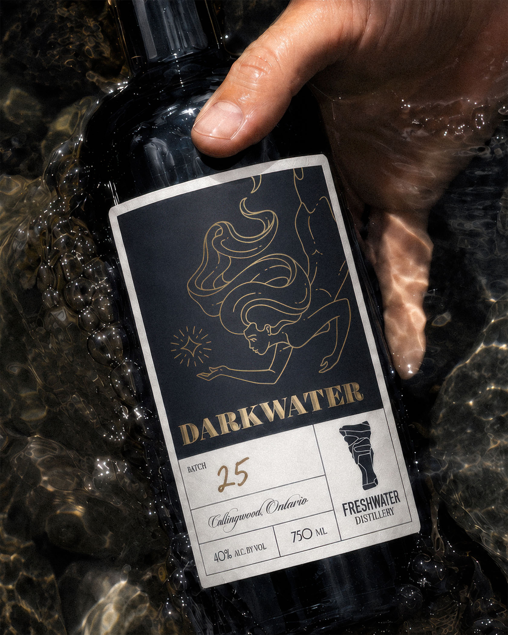 Darkwater bottle held in shallow water, featuring gold foil illustration and Freshwater Distillery packaging design.