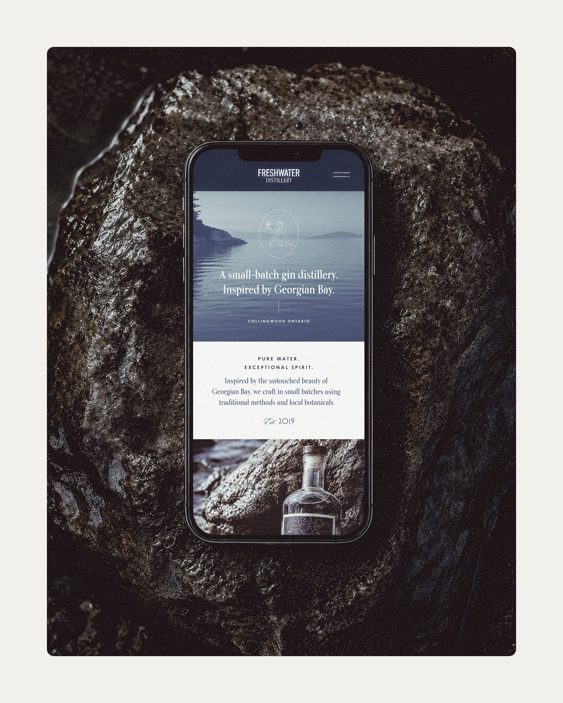 Freshwater Distillery mobile website displayed on a smartphone resting on a damp rock.