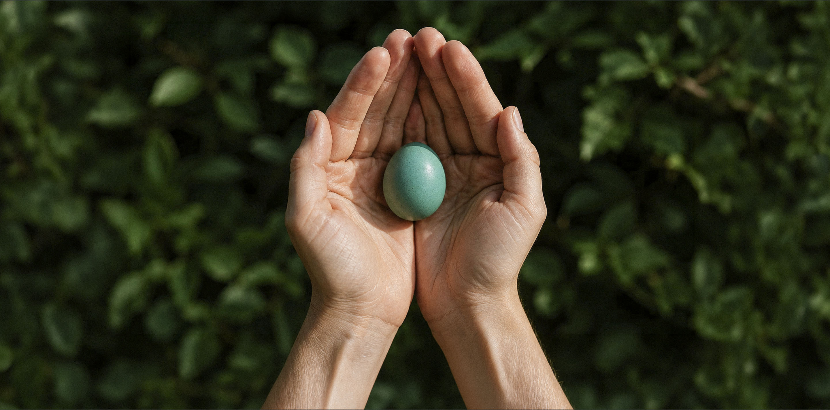 Two hands holding a smooth blue-green stone against a leafy natural background.